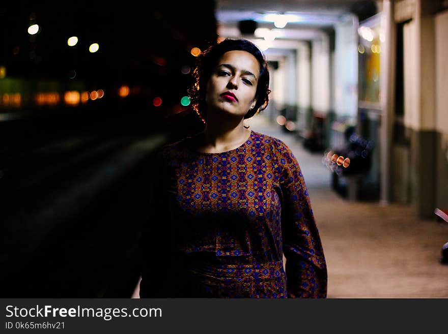 Woman in Brown and Purple Long-sleeved Shirt Standing Outside White Building during Nighttime