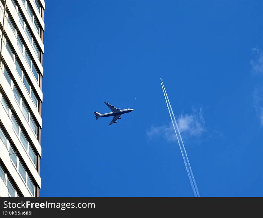 Low-angle Photography of White Plane on Mid-air Near White Concrete Building and White Contrail