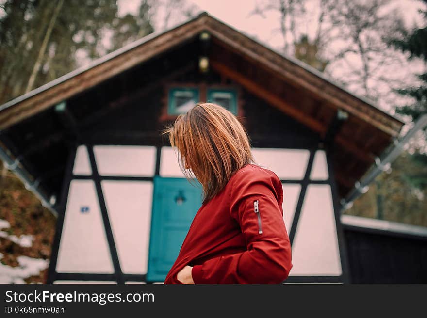 Woman in Red Jacket Standing Near Brown and White Wooden House