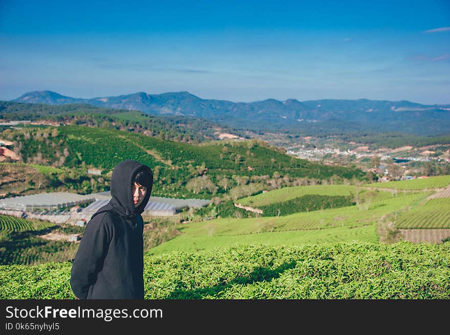 Man Wearing Hoodie Taking Picture With Mountain and Field Photography