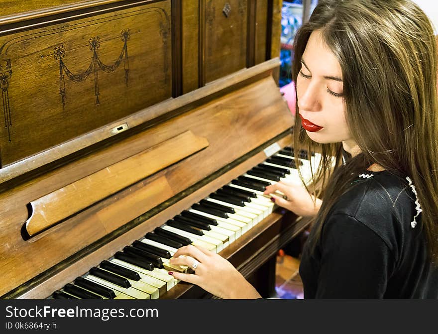 A young blonde woman with colored nails playing a very old piano with ivory keys, looking down with closed eyes. A young blonde woman with colored nails playing a very old piano with ivory keys, looking down with closed eyes.