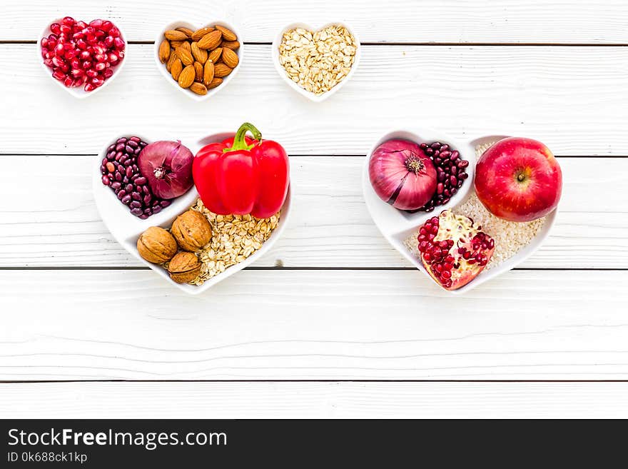 Diet for healthy heart. Food with antioxidants. Vegetables, fruits, nuts in heart shaped bowl on white wooden background