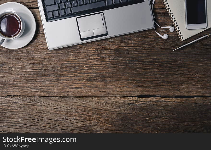 Office wooden desk with pen, notepad, coffee cup, smartphone and earphones. Top view with copy space