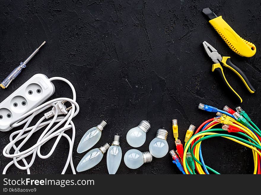 Electrical repair. Bulbs, socket outlet, cabel, screwdriver, pilers on black background top view copy space