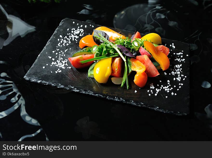 Sliced vegetables on a wooden board in a restaurant, cucumbers, tomatoes, peppers, lettuce leaves.