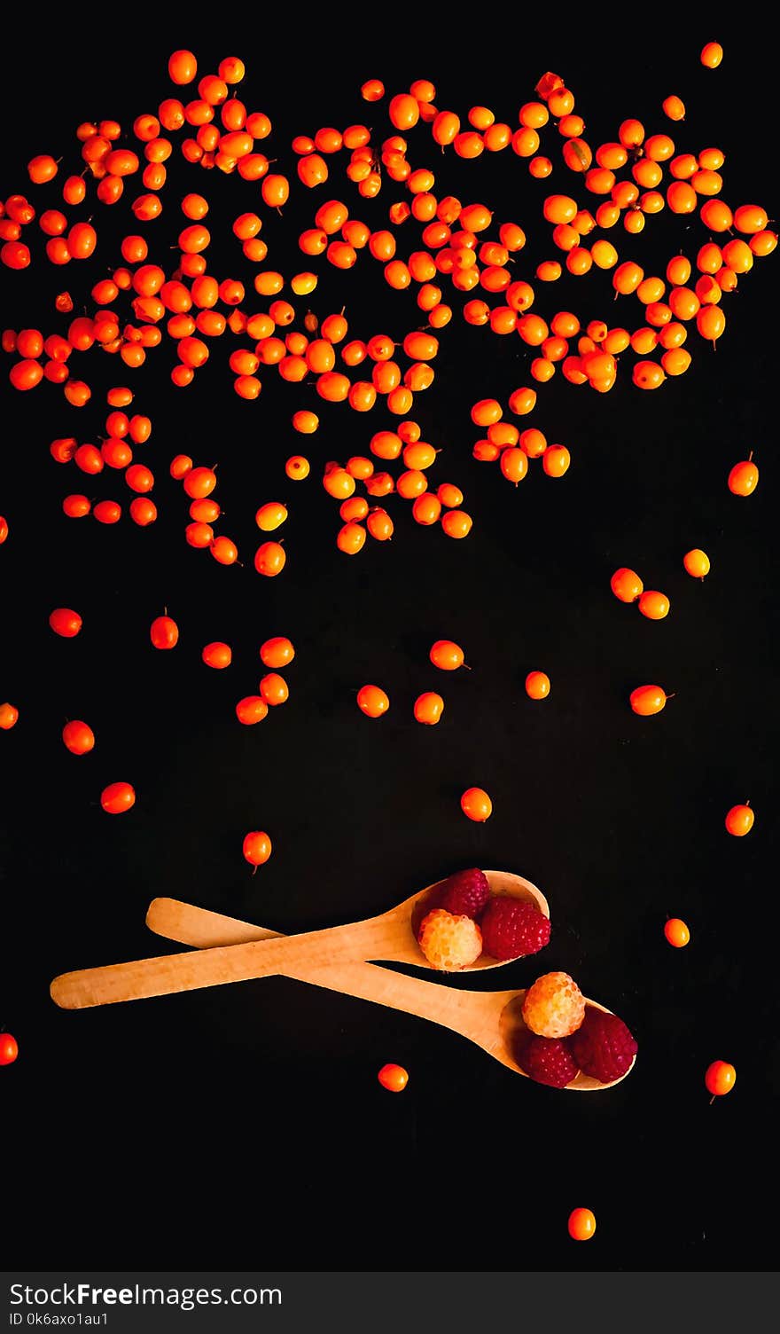 Orange sea-buckthorn background, isolated on a black background, falling down. Wooden spoons with raspberries and sea-buckthorn berries, close-up, natural light, top view