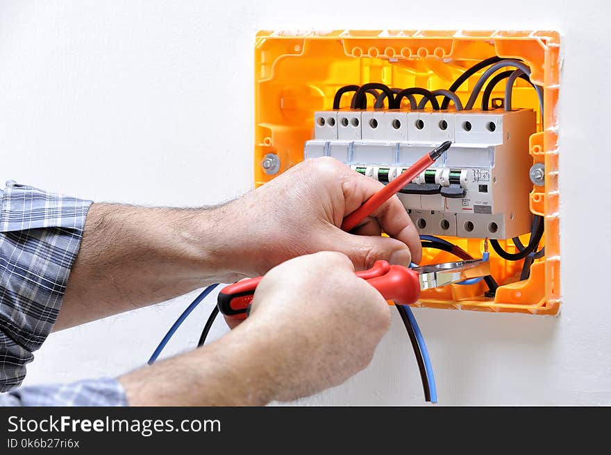 Electrician technician working on a residential electric panel, he inserts the cable in the magnetothermic switch terminals. Electrician technician working on a residential electric panel, he inserts the cable in the magnetothermic switch terminals