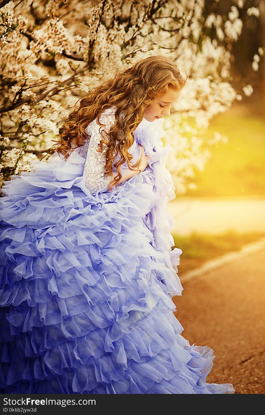 Adorable little girl in blooming cherry tree garden on beautiful spring day.