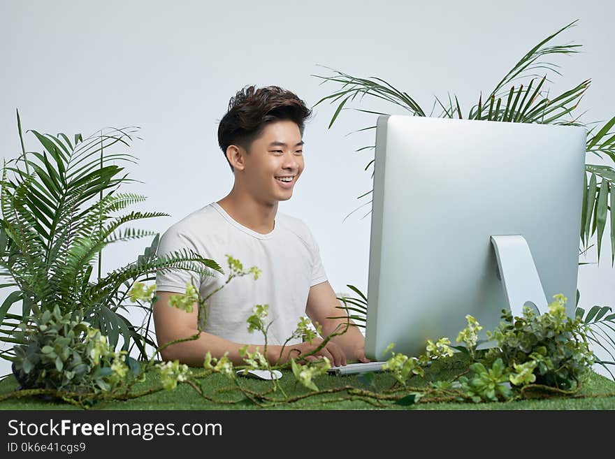 Happy excited Vietnamese young man working on computer with various plants around his workplace. Happy excited Vietnamese young man working on computer with various plants around his workplace