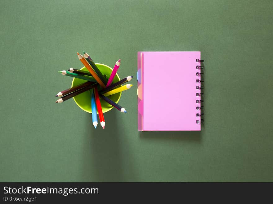 Set of colored pencils and a pink notebook, top view