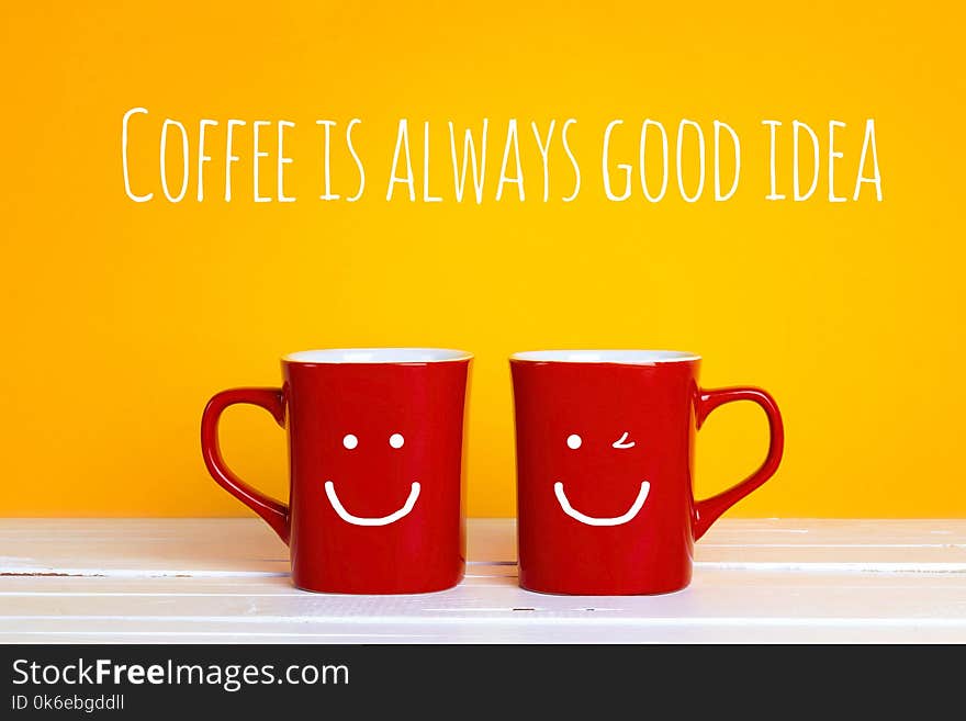 Two red coffee mugs with a smiling faces on a yellow background with the phrase Coffee is alwayas good idea. Happy coffee mugs.