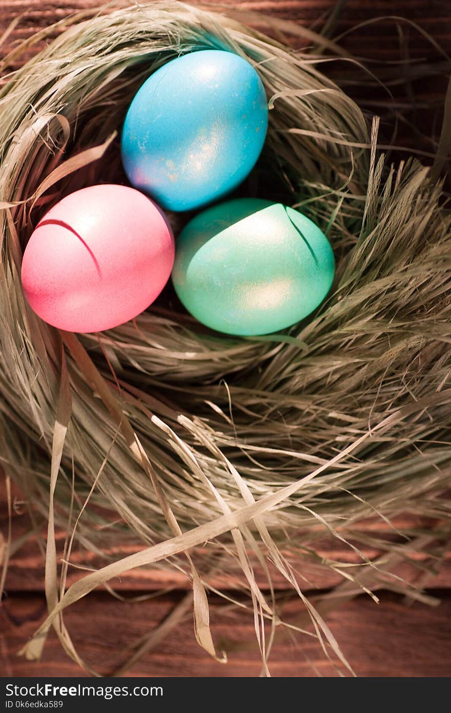 Colorful easter eggs in basket in the hay of the green grass straw bundle dietary delicious gift on wooden table. Top view with copy space. Colorful easter eggs in basket in the hay of the green grass straw bundle dietary delicious gift on wooden table. Top view with copy space