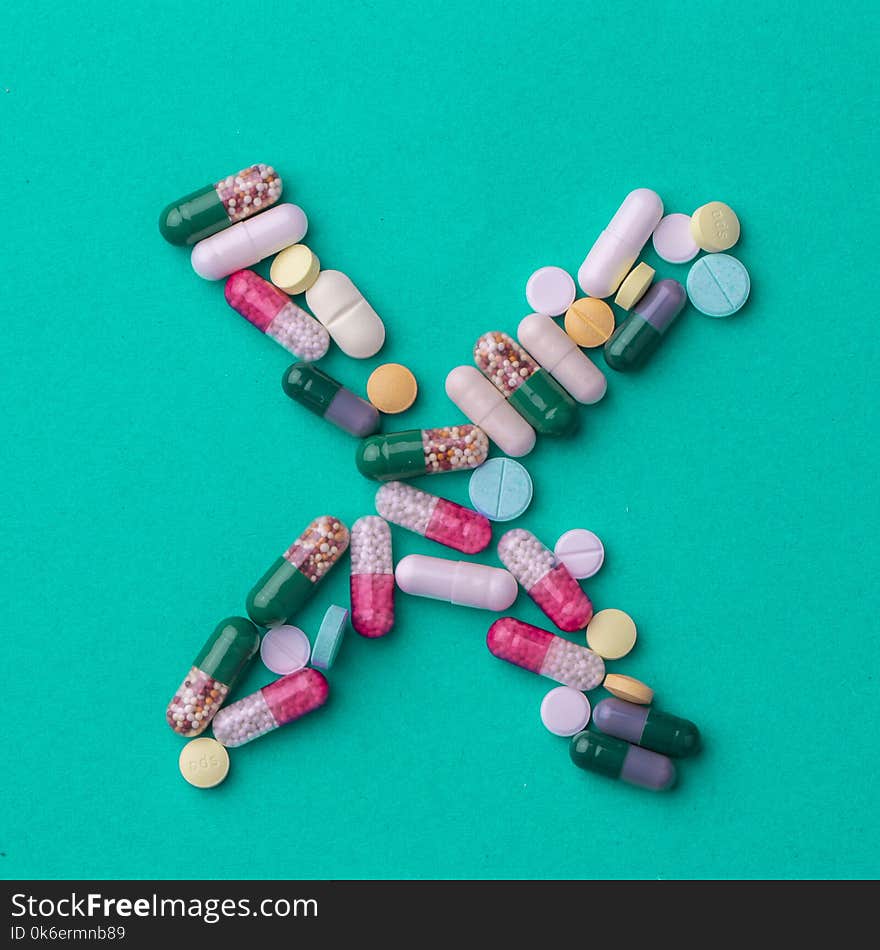 Pills laid out in the shape of a cross or X on a green background. Conceptual for pharmaceutical production.