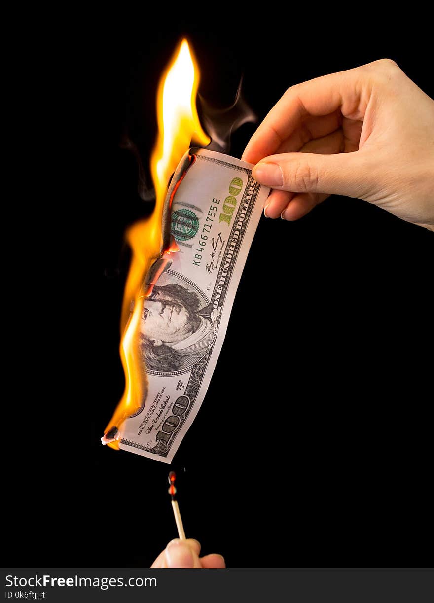 One hundred dollars burn in the hand on a black background .