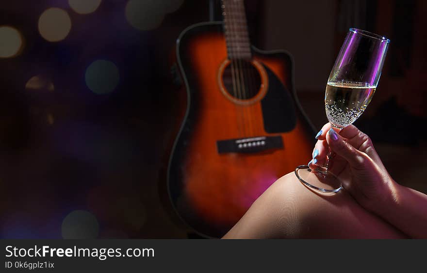 Female hand holding a glass of champagne on dark background with acoustic guitar