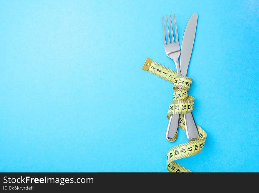 Diet menu in the restaurant or cafe. The fork and knife are wrapped in yellow measuring tape on blue background. Copy space for text