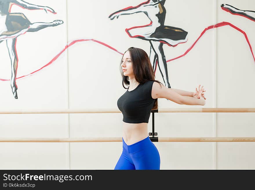 Cute young girl wearing black top and blue pants doing physical exercises warming up. Physical activity concept