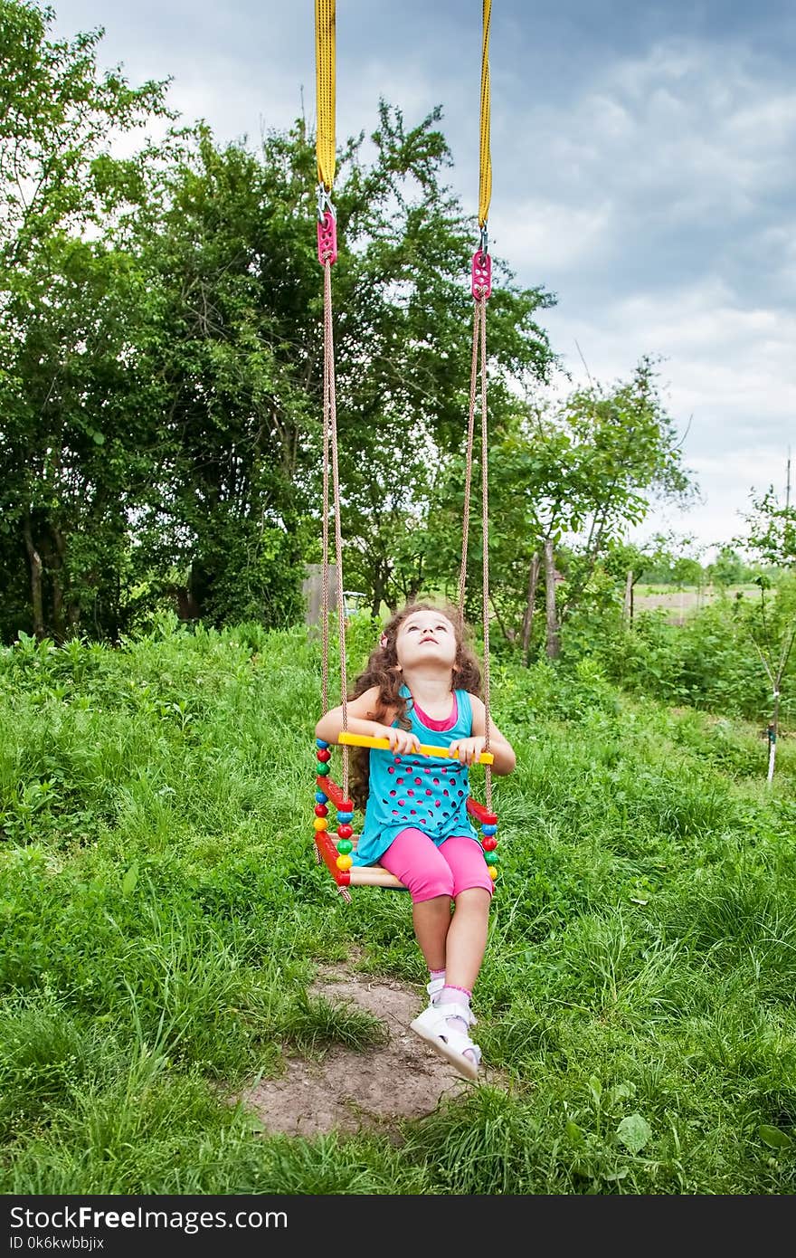Happy baby girl having fun on swing on summer day, sitting on swing looking up at the sky. Happy baby girl having fun on swing on summer day, sitting on swing looking up at the sky