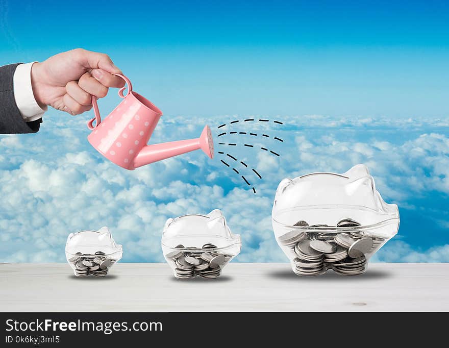 Transparent piggy bank filled with coins on wood background.Saving investment concept.Watering can and money growth drawn concept