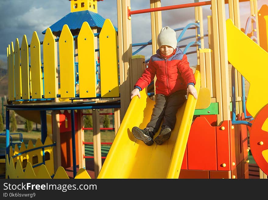 Happy little boy have fun and sliding on colorful modern playground in a park.