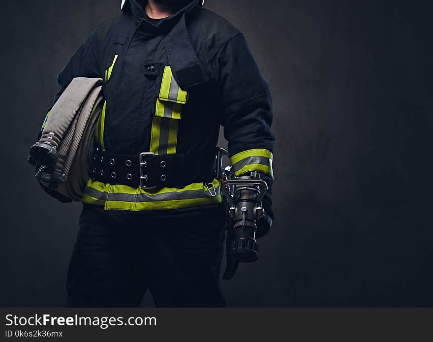 Studio portrait of a firefighter in uniform holds fire hose.