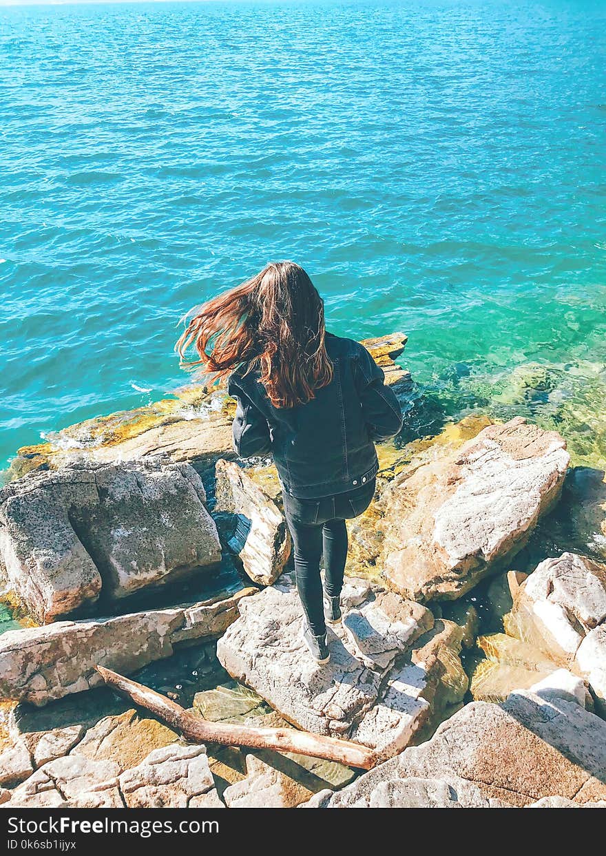 Woman Wearing Denim Jacket Standing on Rock Near Body of Water