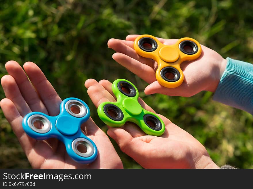 Spinner of different colors lie in the hands of children against the background of grass