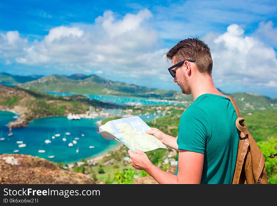 Young Tourist Man With Map Background Of English Harbor From Shirley Heights, Antigua, Paradise Bay At Tropical Island