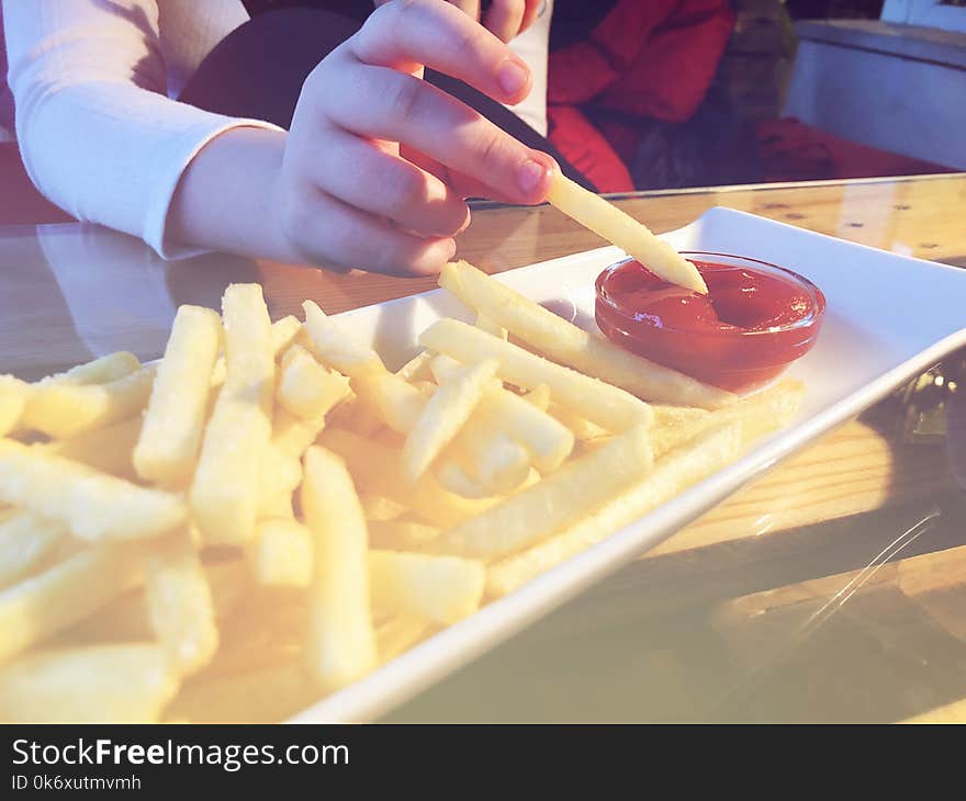 French Fries in the white plate with red cachup, girl hold one piece of french fries in her fingers.