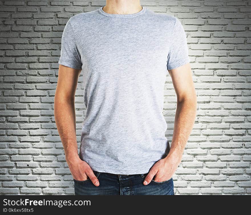 Man wearing blank grey shirt on brick wall background. Advertisement and design concept. Mock up. Man wearing blank grey shirt on brick wall background. Advertisement and design concept. Mock up