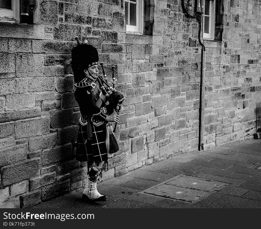 Person Using Bagpipes Near Wall in Grayscale Photography