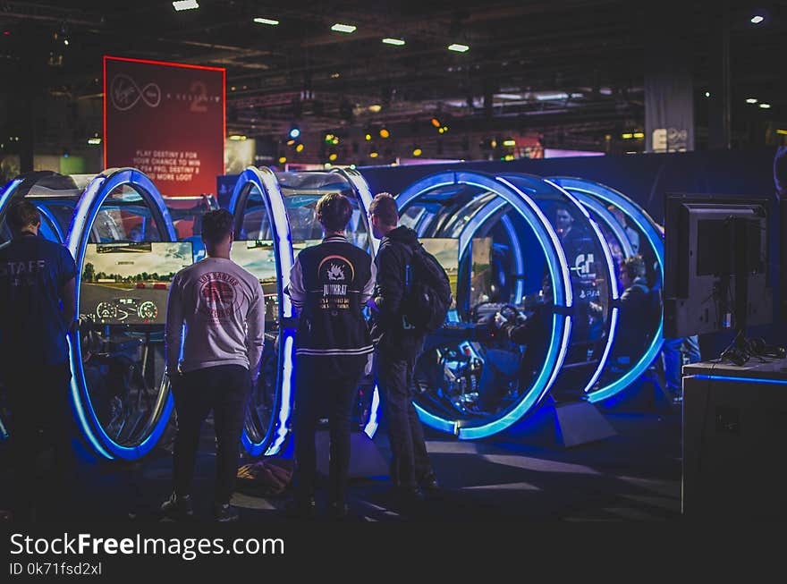 Three Men Standing in Front of Racing Arcade Machines