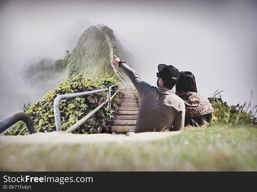 Photography of Couple Sitting on Green Grass Near Bridge