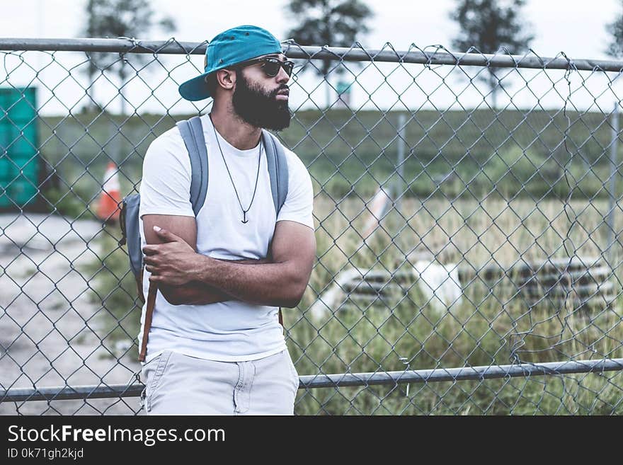 Selective Focus Photography of Man in White Crew-neck T-shirt Leaning on Gray Metal Chain Fence