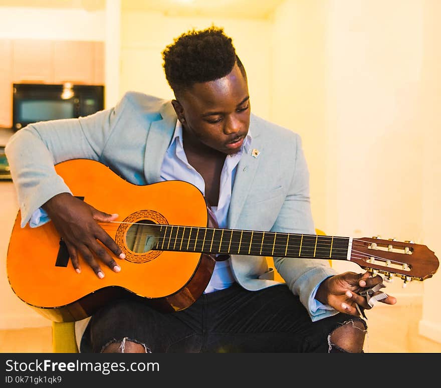 Man Wearing Blue Coat and Black Distressed Bottoms Holding Brown Classical Guitar