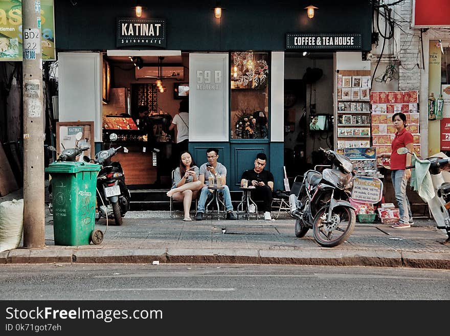 Three People Sitting on Chairs Outside Coffee & Tea House Near Motorcycles