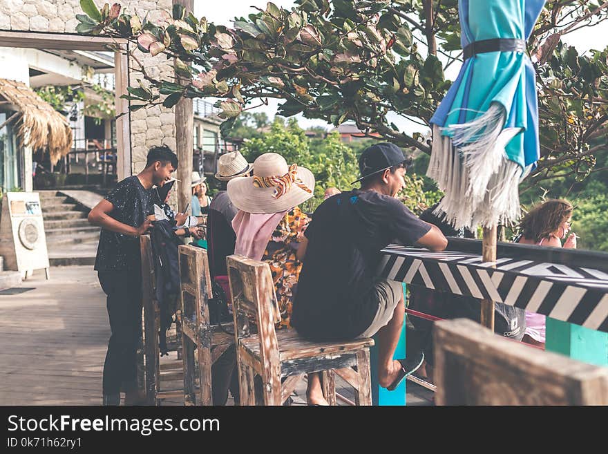 Man in Black T-shirt and Brown Shorts Sitting on Brown Wooden Bar Stool