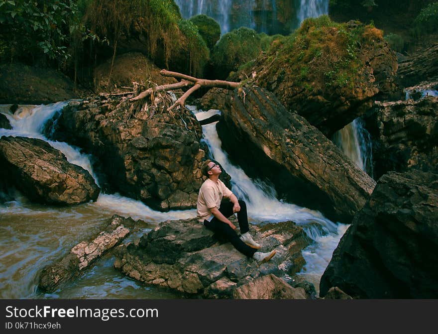 Photo of Man Sitting on Gray Rock Surrounded by Water Falls