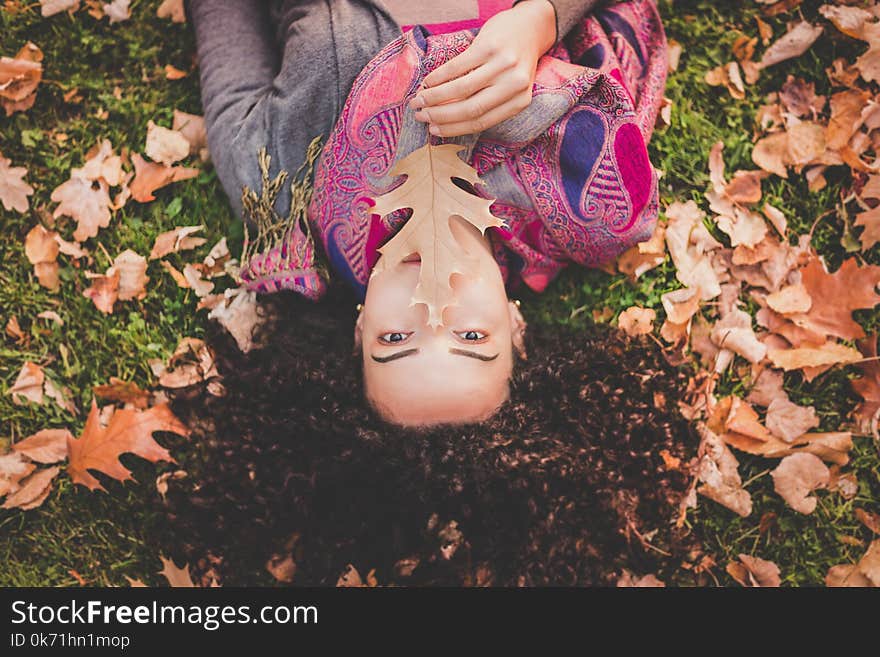 Woman Lying Down On Green Grass Field Holding Brown Leaf