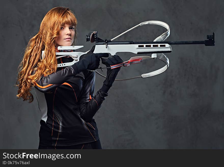 Redhead female Biathlon champion aiming with a competitive gun.