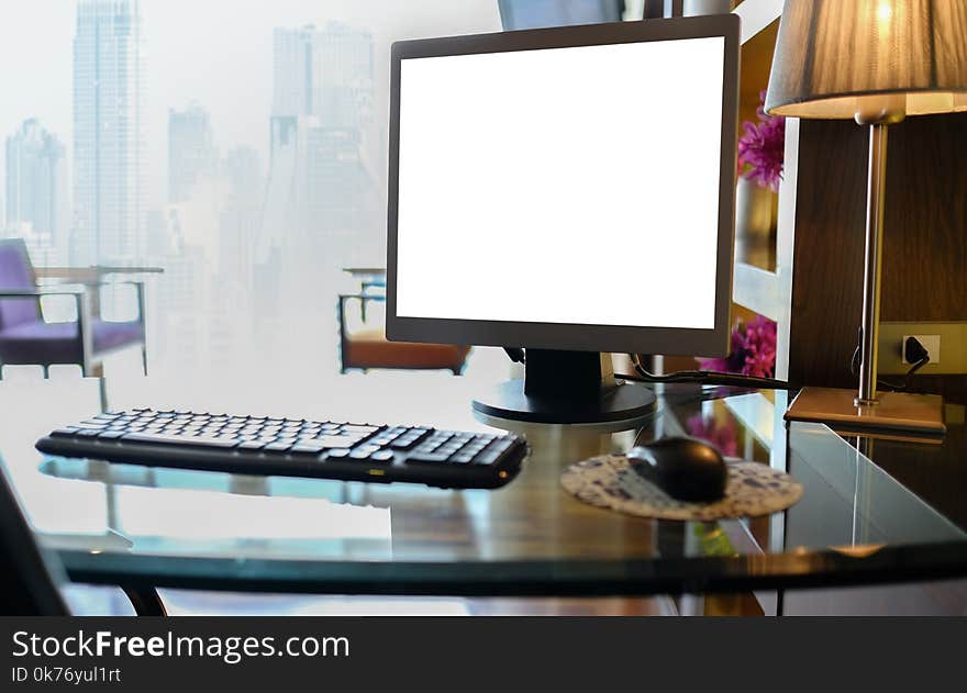 Blank desktop computer with keyboards and other accessories on the desk in a warm light room with clipping path on screen. mock up