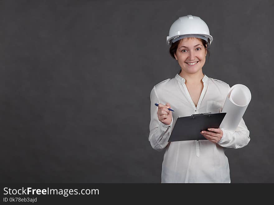 Young female architect in a protective helmet makes notes on the project with a paper in hands.