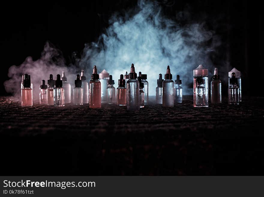 Vape concept. Smoke clouds and vape liquid bottles on dark background. Light effects. Useful as background or vape advertisement o