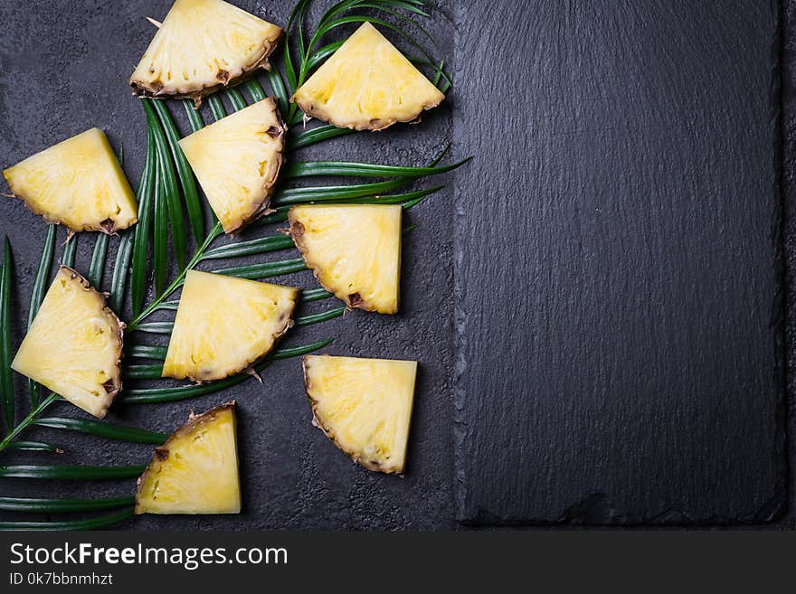 Sliced pineapple and palm branch on a black background.