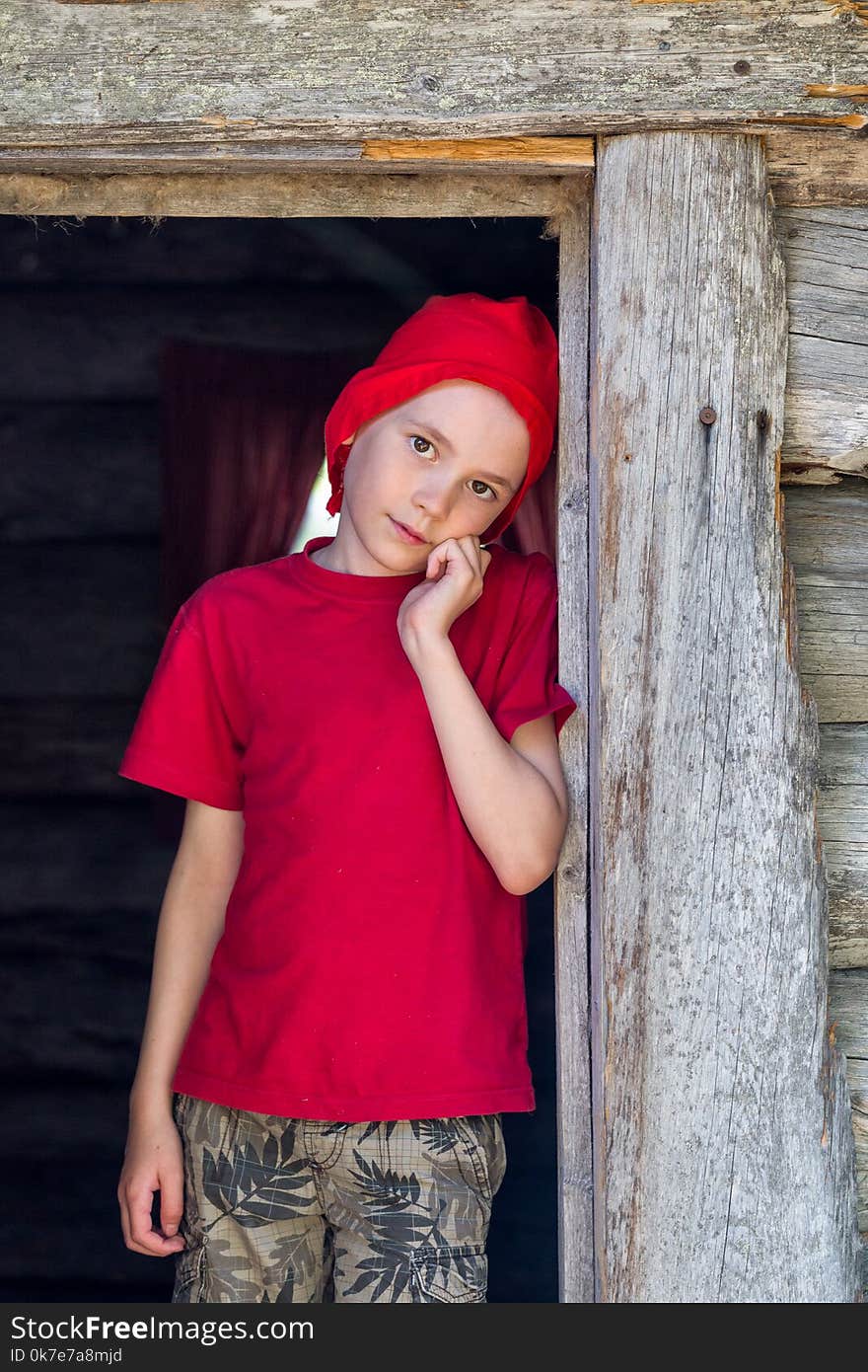 The boy in the red Christmas hat stands in the old house door