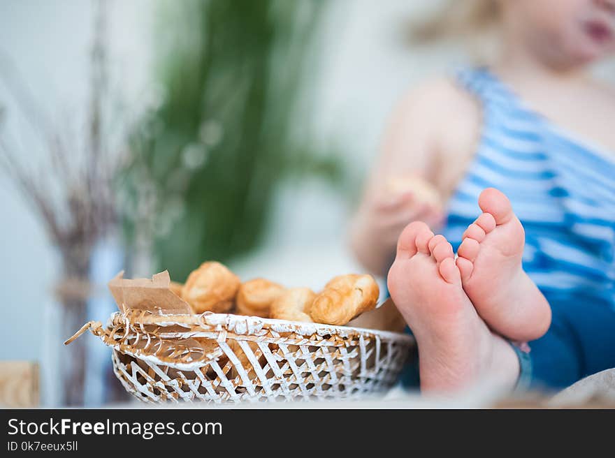 A little girl in a vest with a vest sits on the table. Focus on children`s legs and a basket with croissants