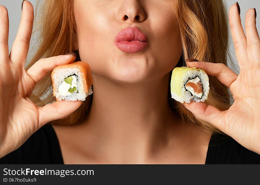 Closeup woman with sushi hold philadelphia rolls in hands show kissing sign on a light gray background