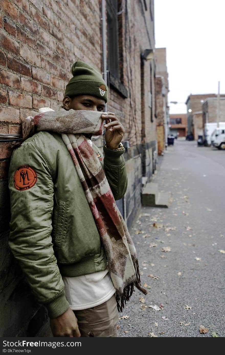 Man Wearing Bubble Jacket With Scarf Leaning on Wall