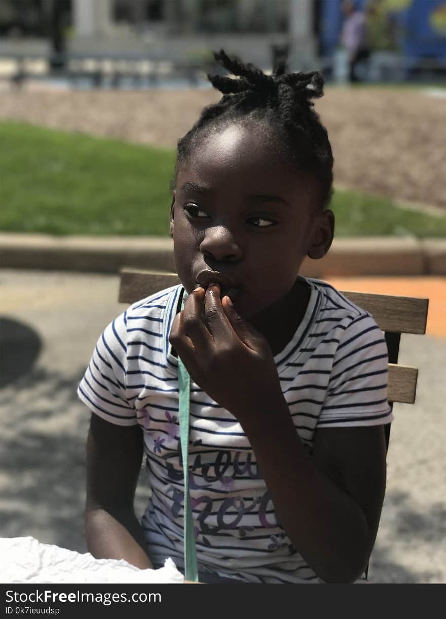 Girl with her fingers in Mouth While Sitting on a Wooden Chair