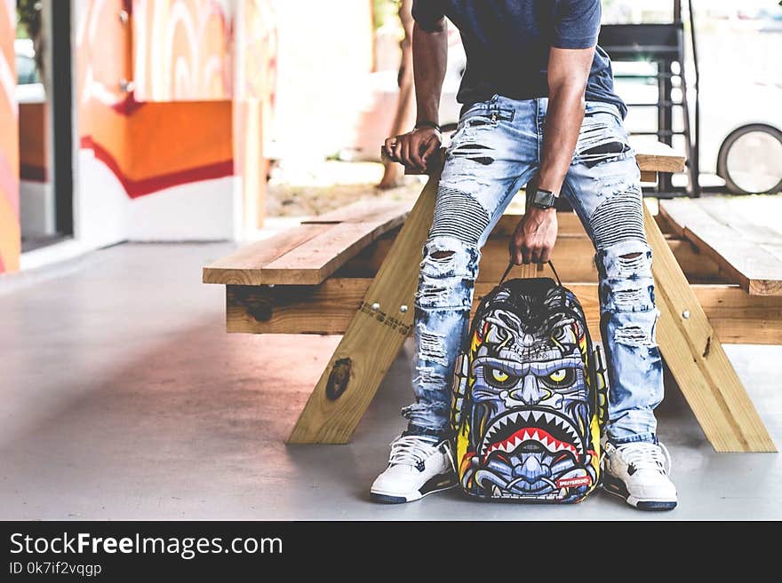 Man Wearing Distressed Denim Pants Holding Multicolored Backpack